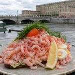Schwedische Räkmacka mit einem großen Berg Garnelen, Ei, Mayonnaise, Dill und Zitrone vor Stockholmer Wasserkulisse